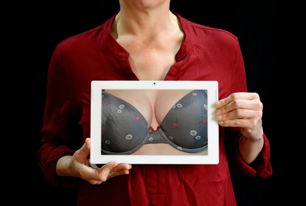 Adult woman in red shirt holding a tablet showing a lingerie closeup, studio shot.