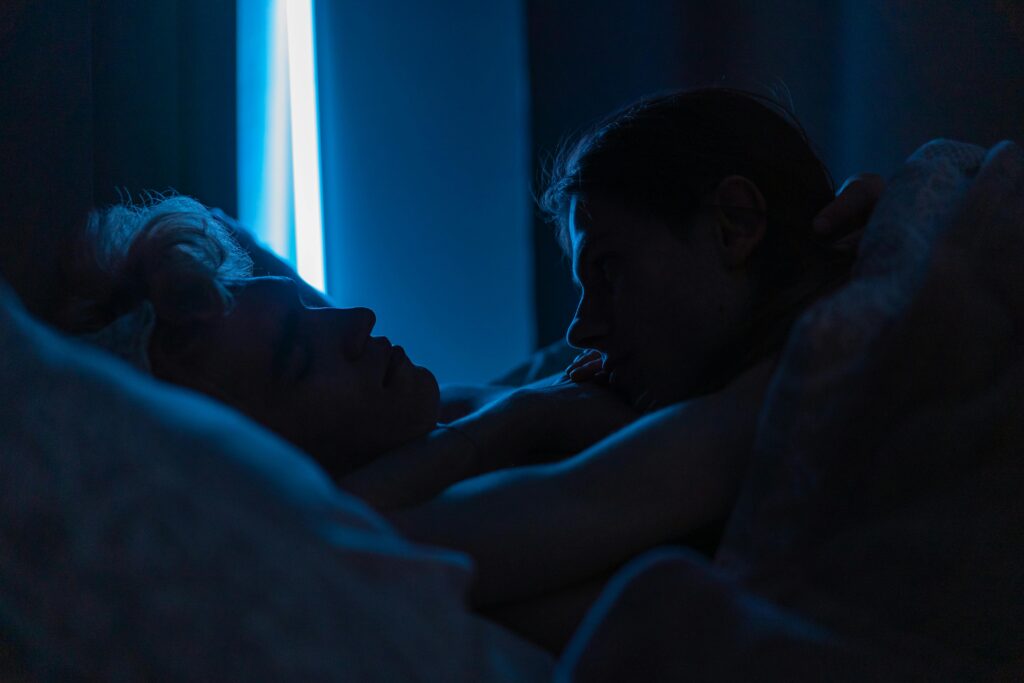 A romantic moment of two men sleeping closely together under soft blue lighting, conveying warmth and affection.